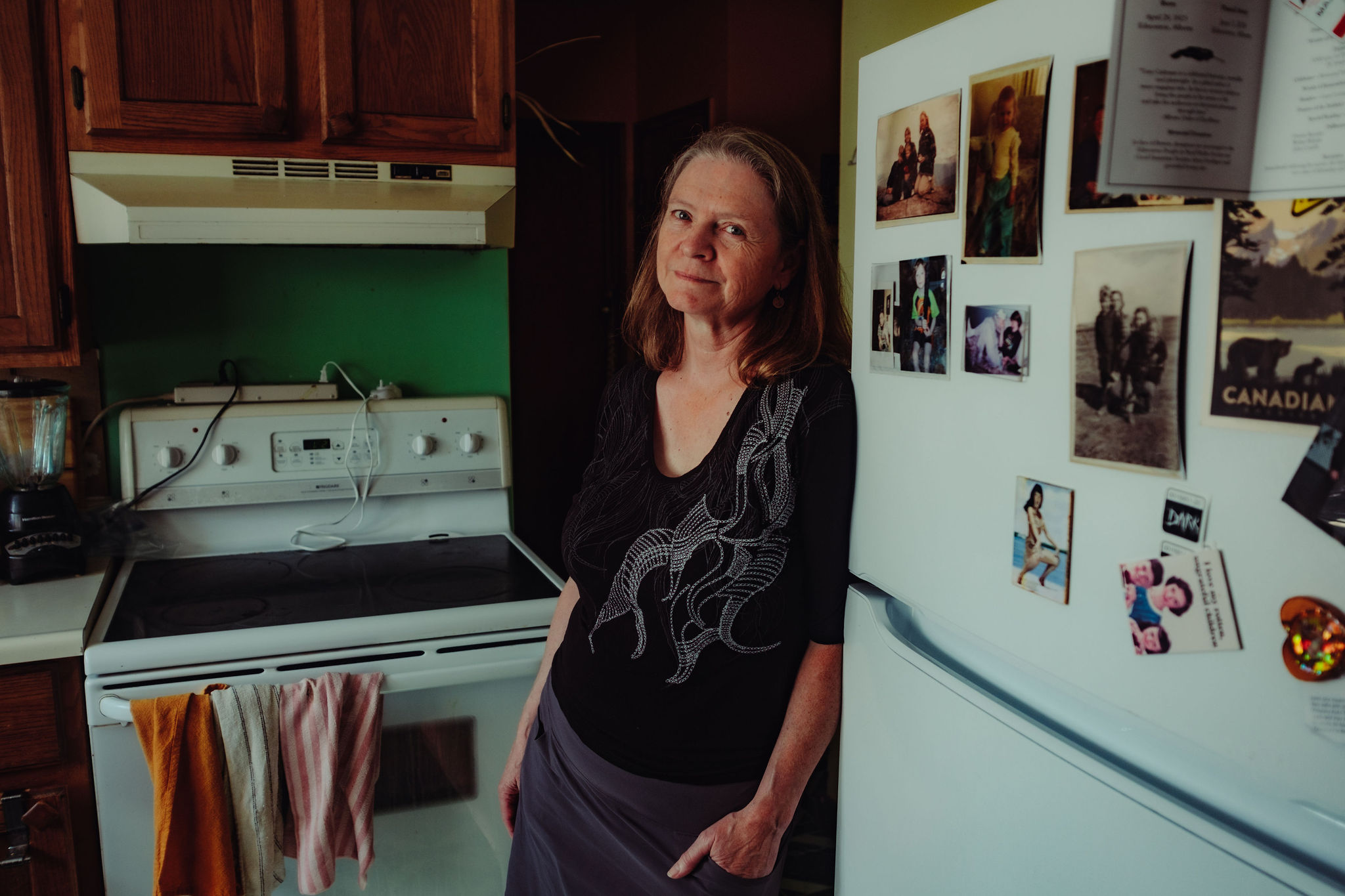 A woman leans against a fridge in a kitchen.