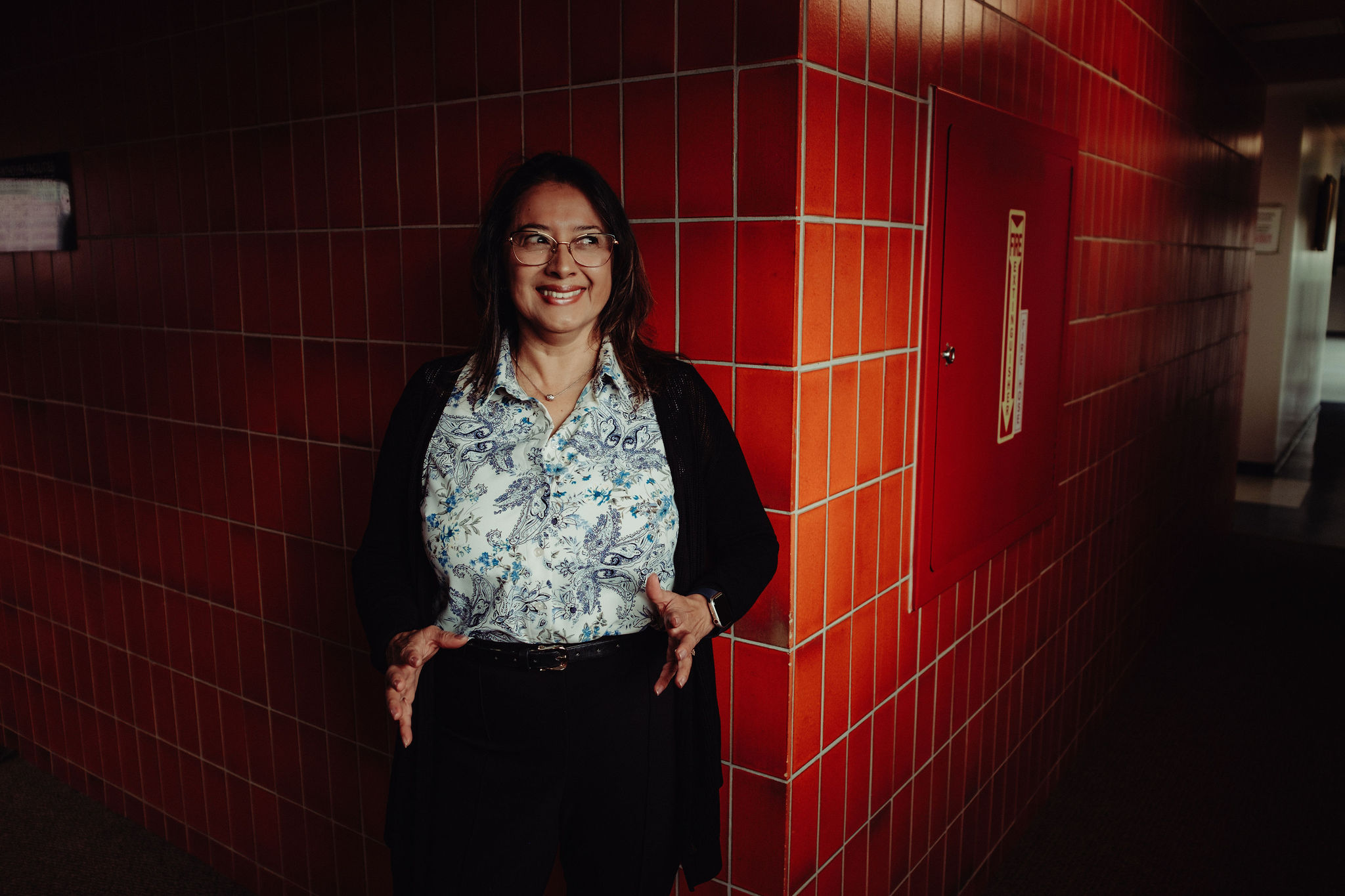 A woman gestures with her hands in front of a brick background.