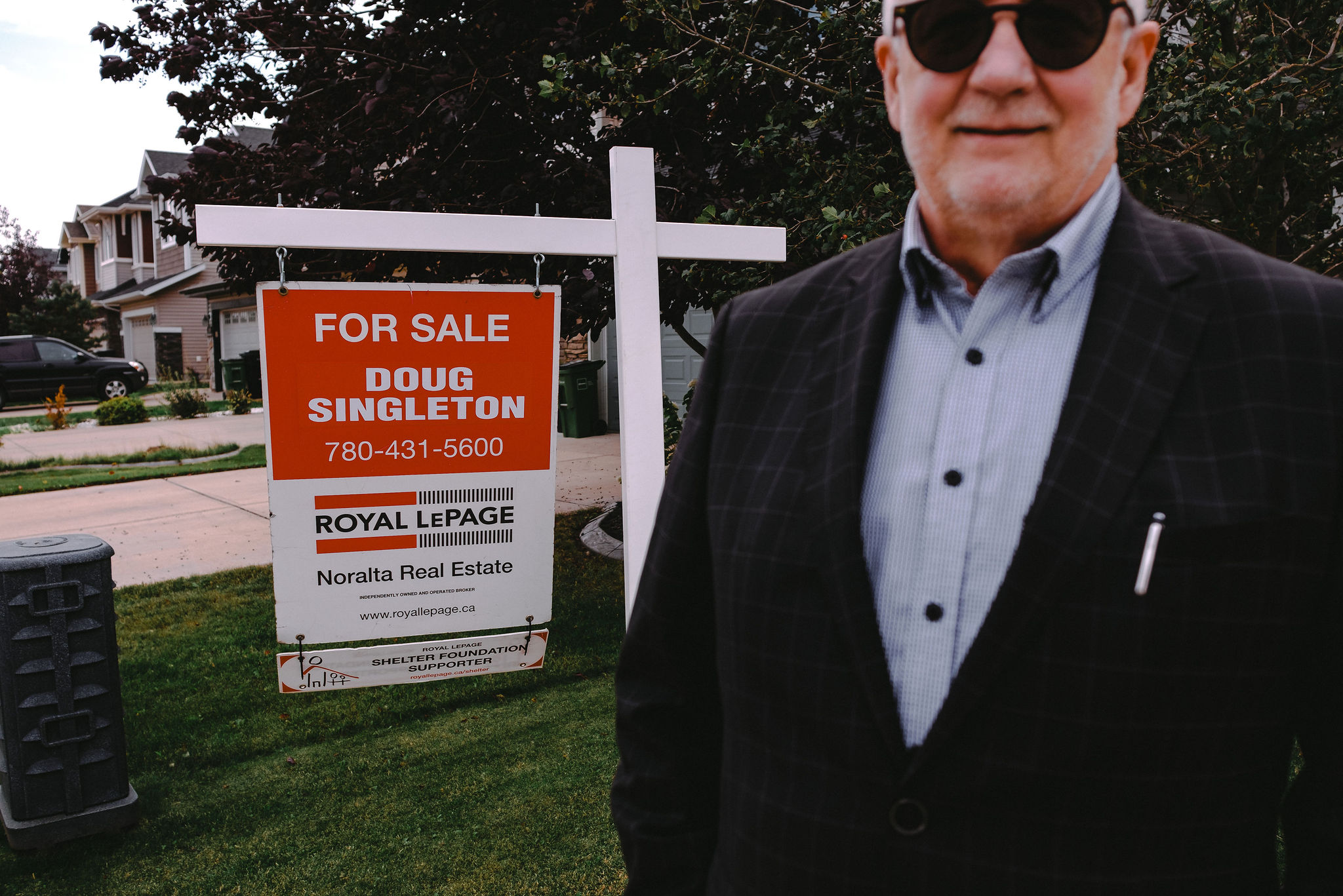 A man stands in front of a For Sale sign.