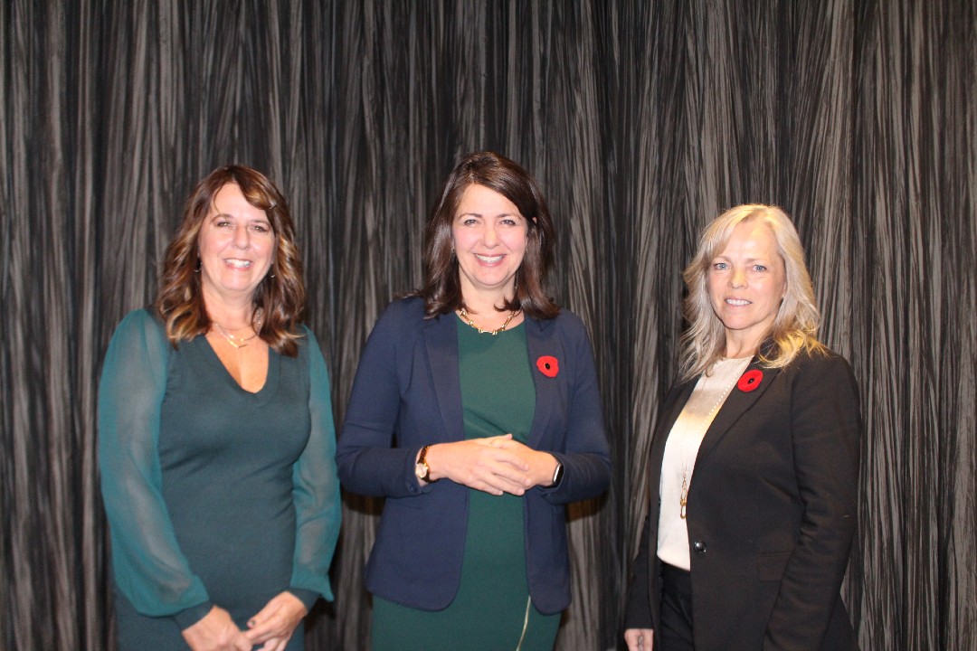 Three people, including Alberta Premier Danielle Smith, pose in business casual attire.