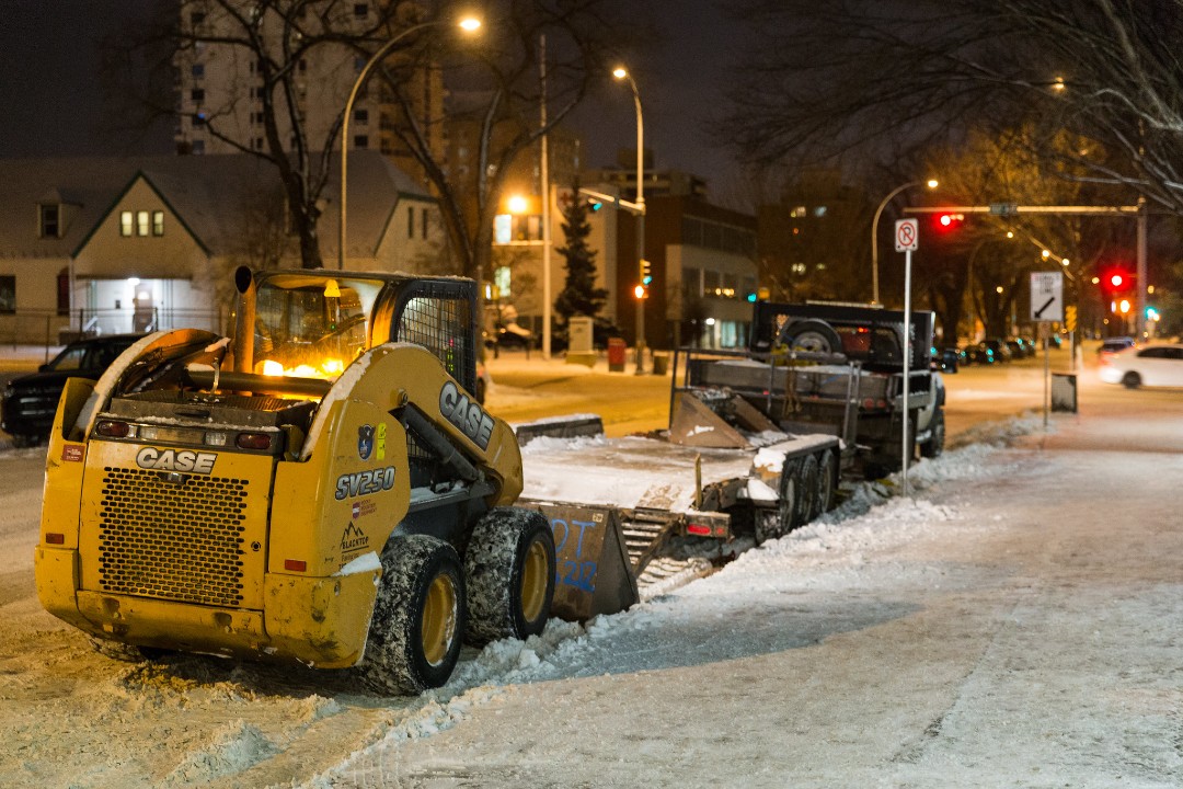 A small Case-brand plow clears snow at night.