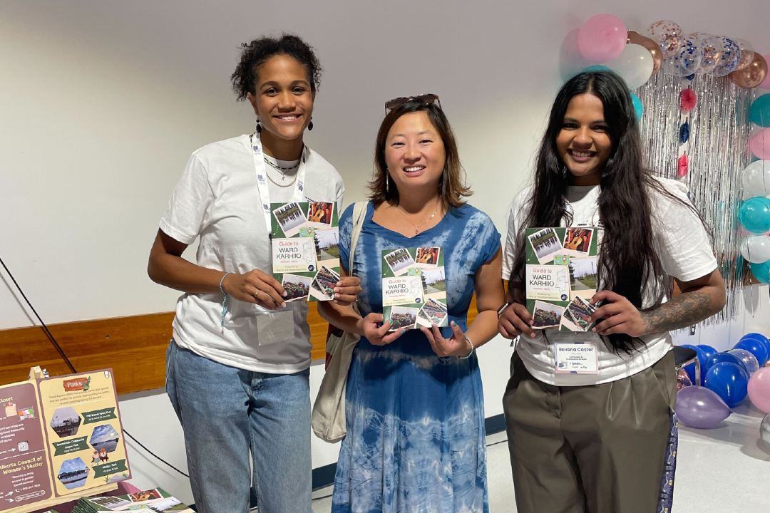 Three people holding booklets smile in a gymnasium.