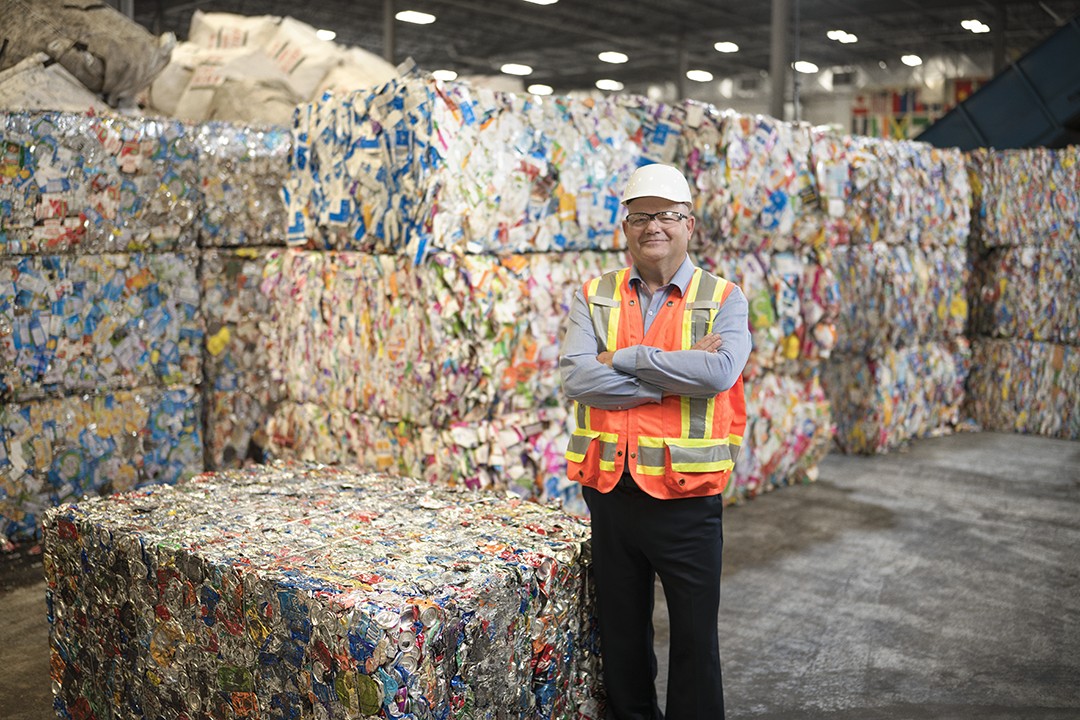 A person in safety gear posts amid cubes of compressed aluminum cans.