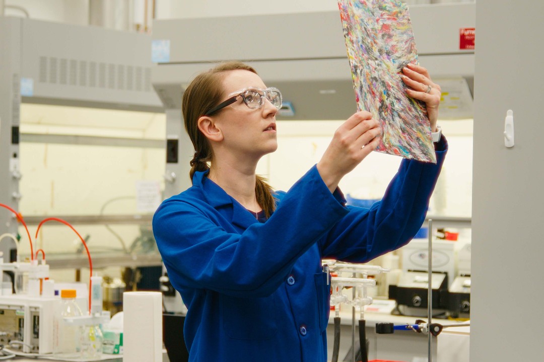 Groups researching how to better recycle the 15 million pouches Albertans consume yearly A scientist in a lab looks up at a colourful object.