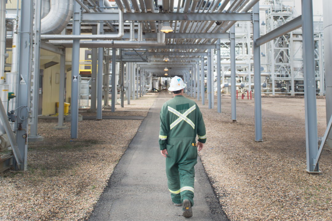 A worker in personal protective equipment faces away from the camera during a walk through an industrial site.