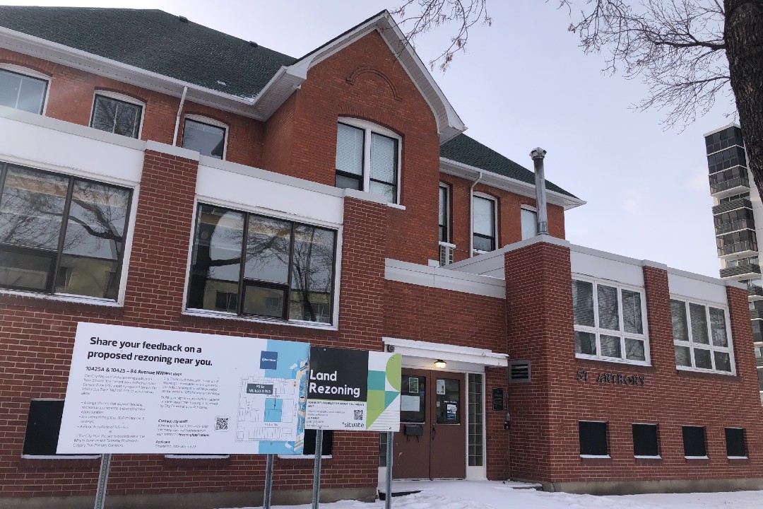 A two-storey red brick building with signs in front describing a rezoning application.