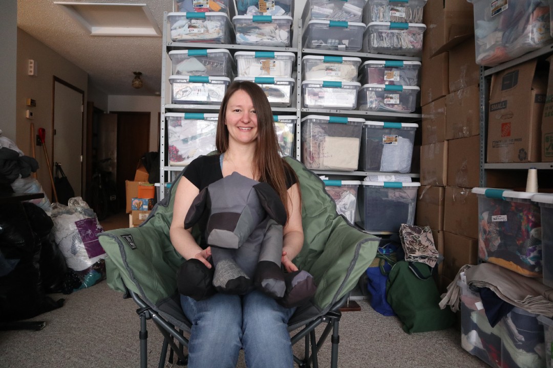 A woman sits on a camping chair holding a stuffed dog.