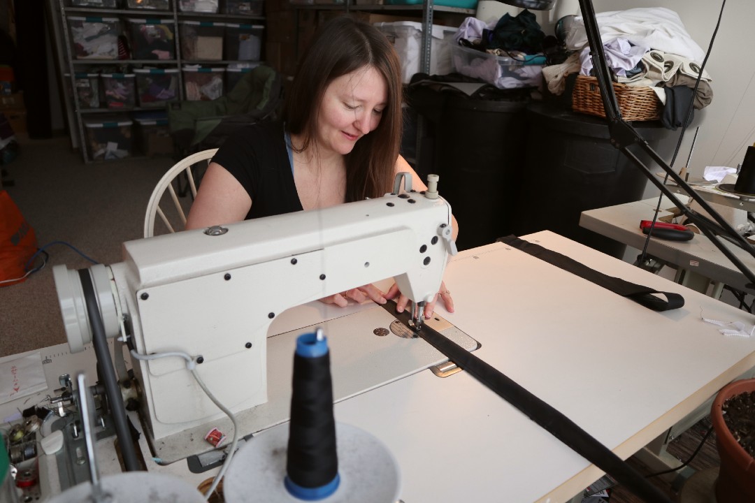 A woman sews a piece of black fabric.