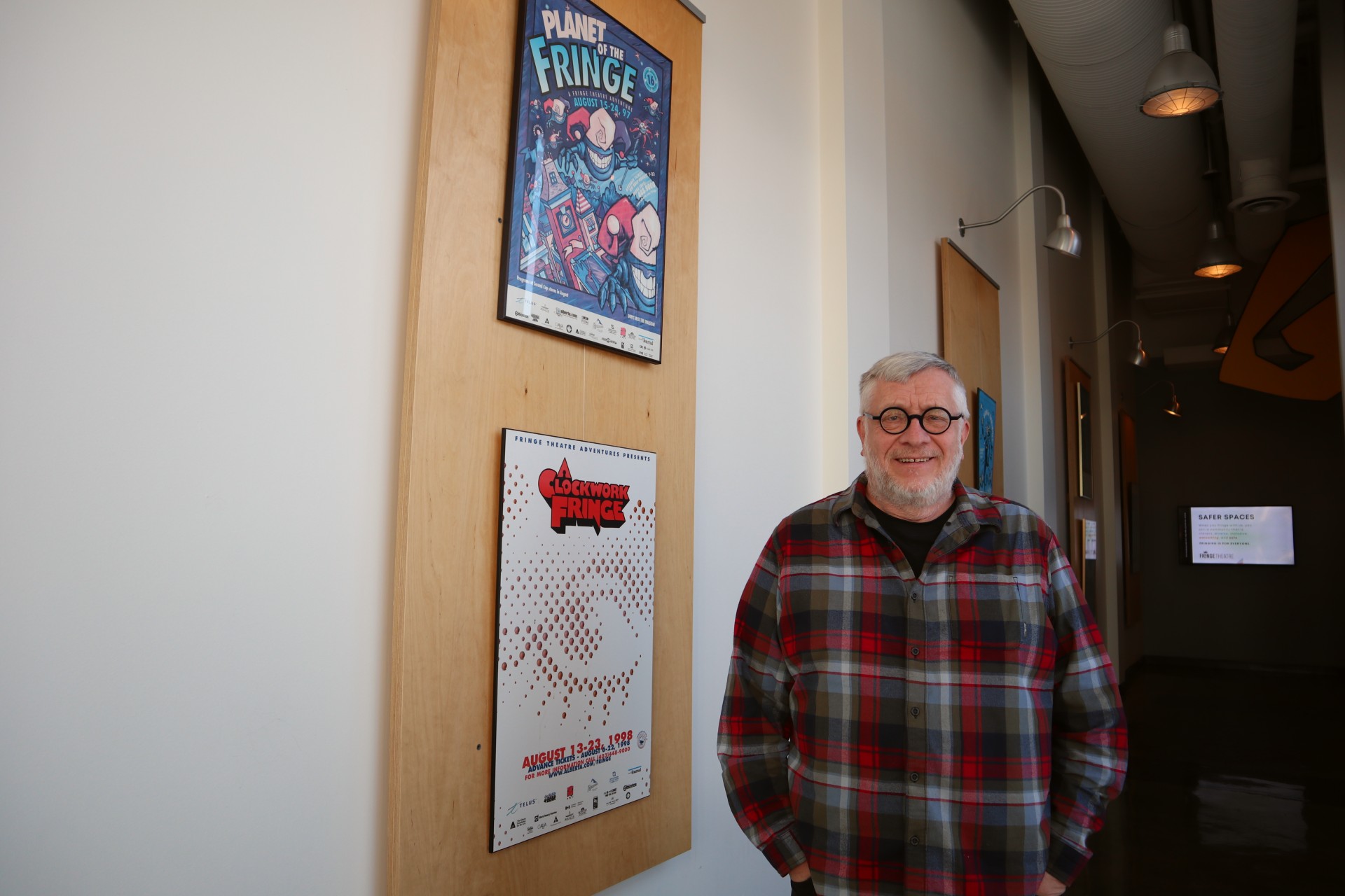 A man in a plaid shirt stands smiling next to Fringe posters.