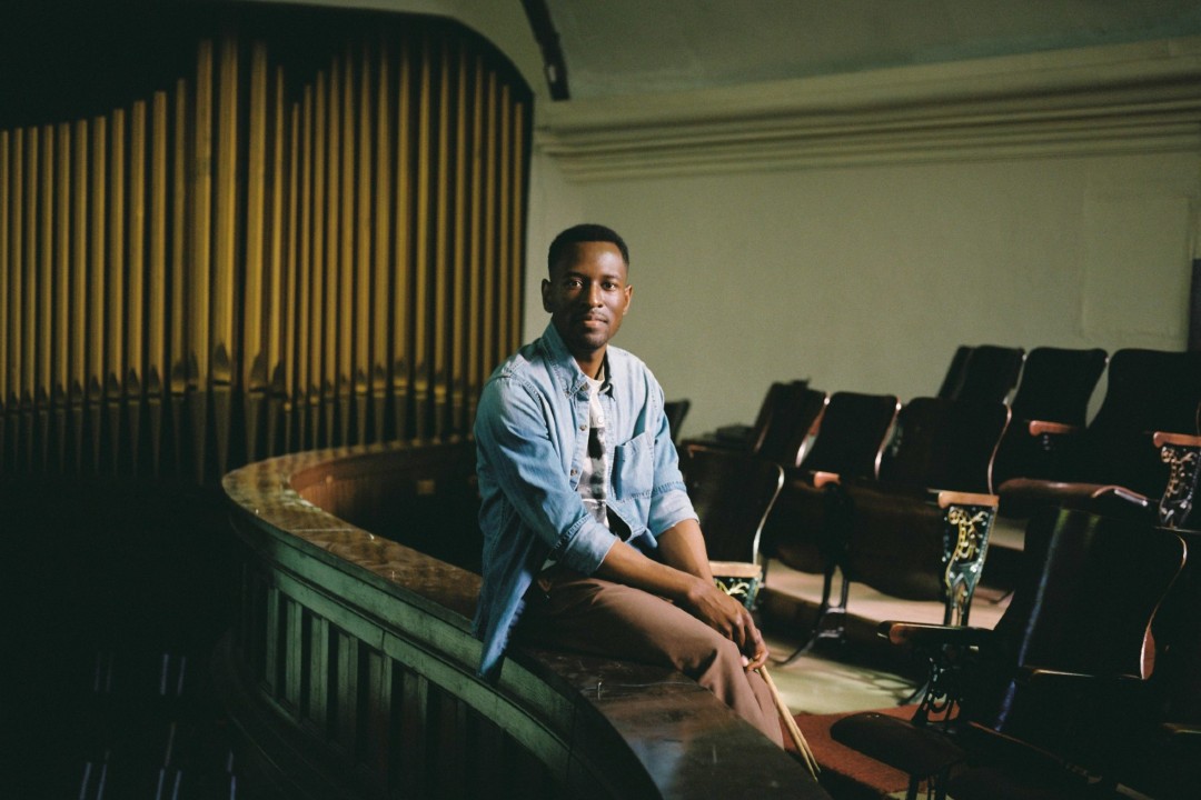 A person sits on a balcony between a pipe organ and a seating area.