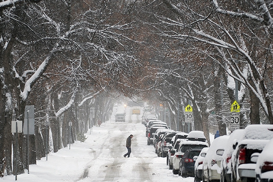 Calls for public engagement: Winter park use, snow and ice control, passenger rail A person crosses a snowy street, cars are parked on the right side