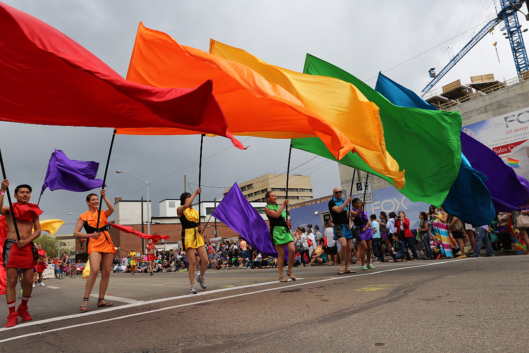 Six people in a line holding single-colour flags that make up the rainbow Pride colours