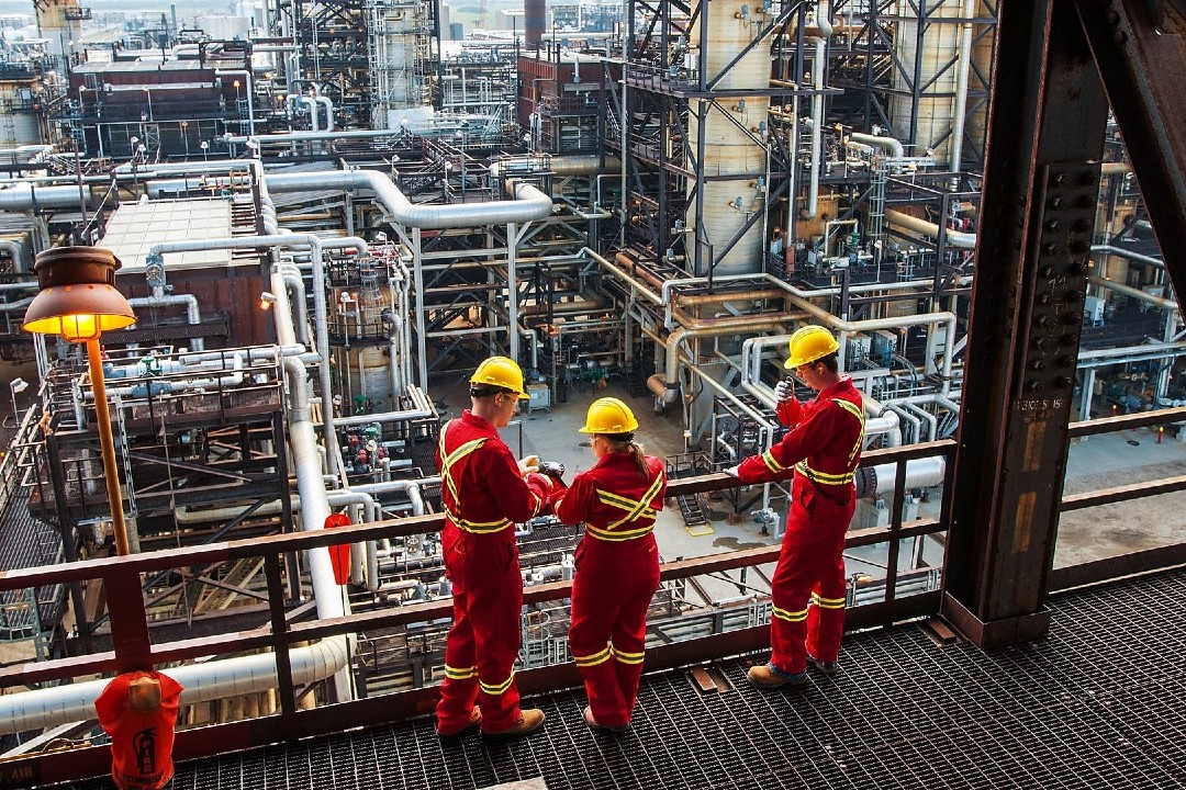Hydrogen Naturally targets capturing carbon and producing hydrogen with waste wood Workers wearing red and yellow safety gear inside an industrial facility.