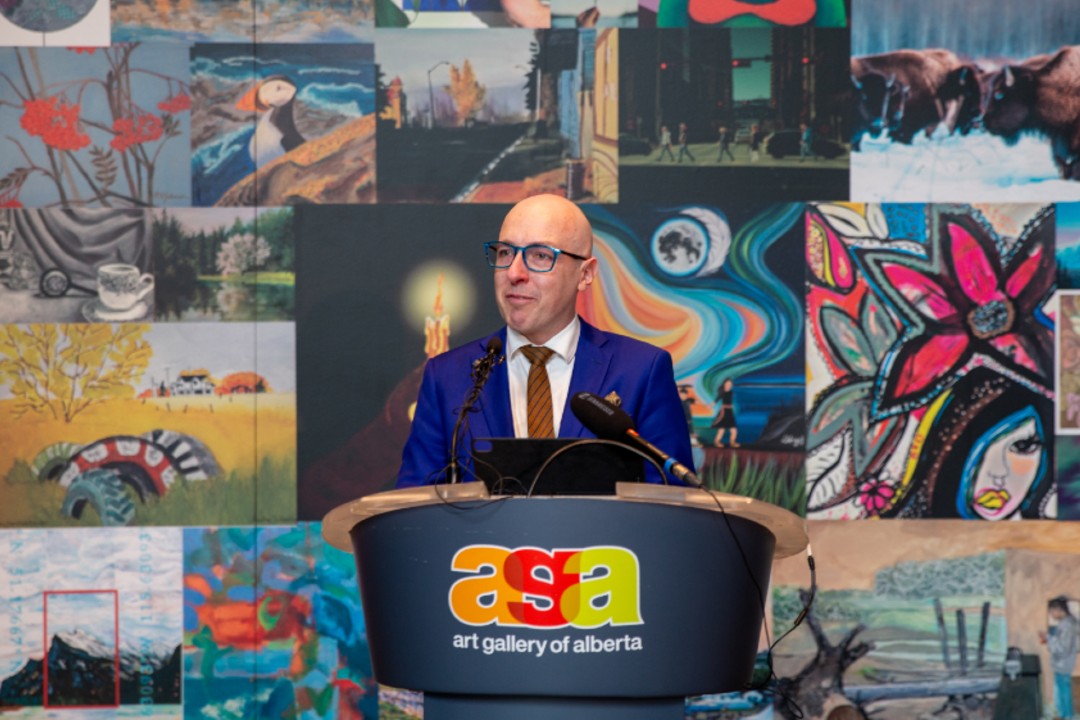 A man stands at a podium in front of colourful artwork.