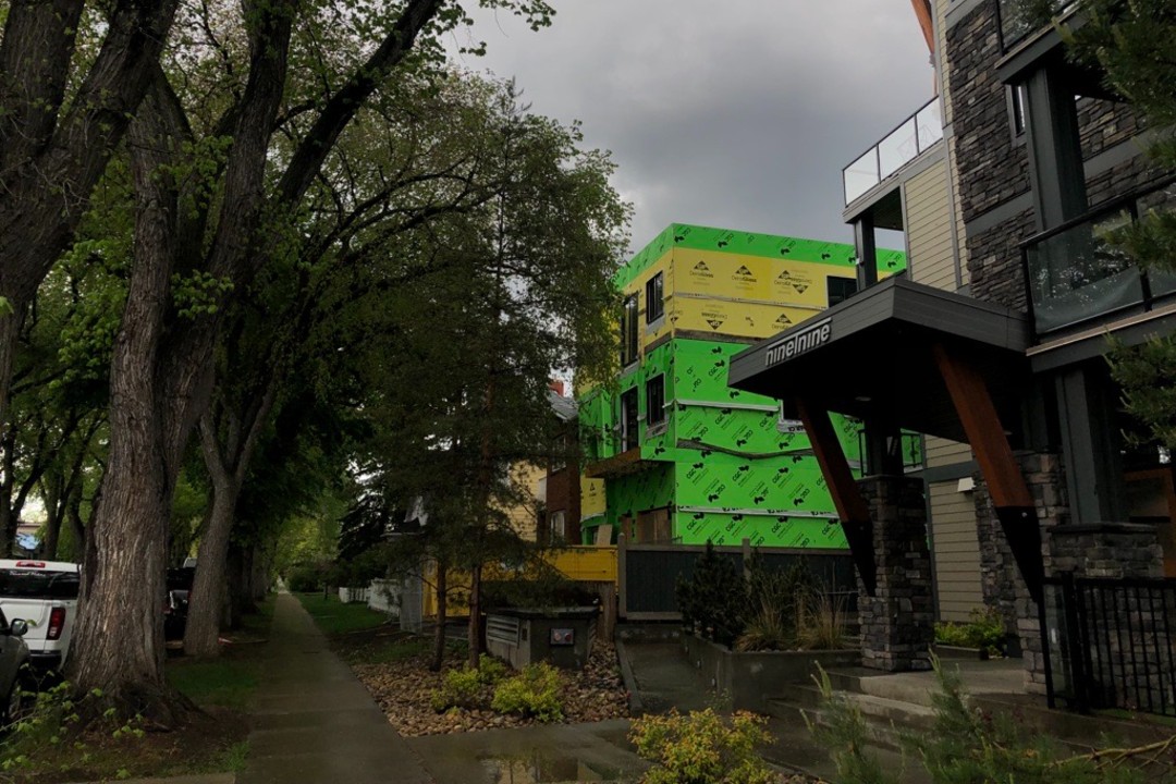 One year after zoning reform, housing surges but sprawl continues A building wrapped in yellow and green under construction surrounded by mature trees and existing homes.