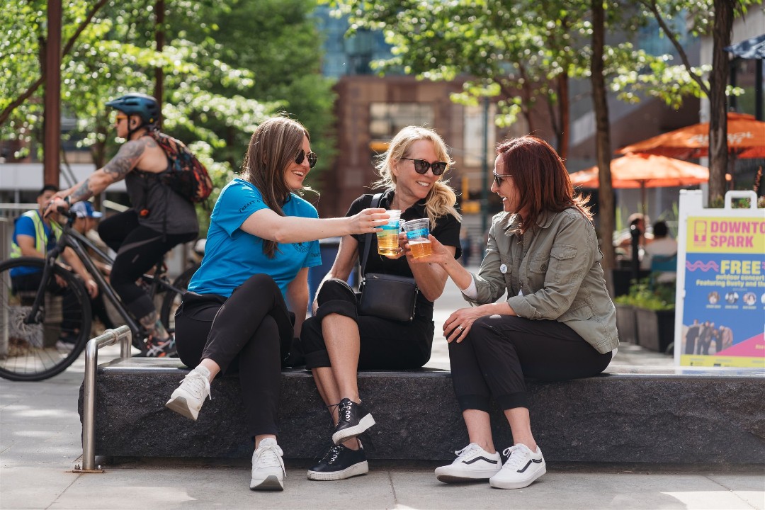 City chose single-use plastics for its entertainment districts despite bylaw and concerns Three seated people smile while toasting with plastic cups on an outdoor bench.