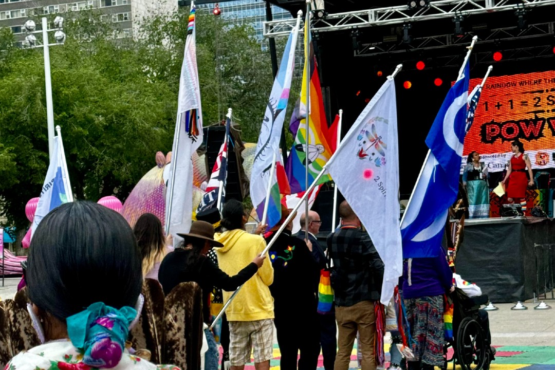 Edmonton 2 Spirit Society to host first solo powwow People wearing brilliant colours carrying an assortment of flags gather in front of an outdoor stage.