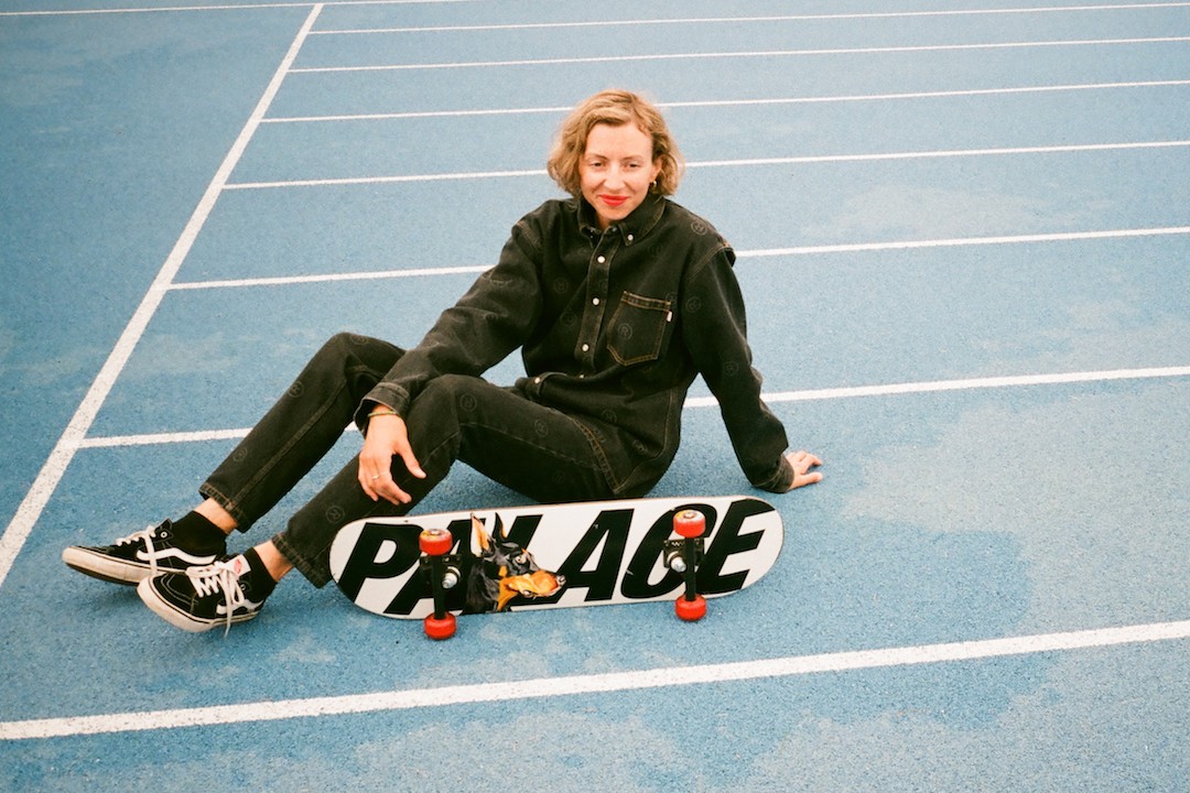 Lexi Pendzich hopes to inspire people to build places with SKATE WORLD event A woman in a matching denim outfit seated on cement with a Palace brand skateboard.