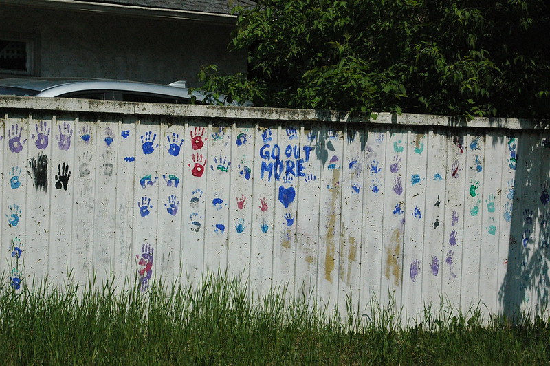 Happenings: June 27, 2025 A fence adorned with colorful handprints and the phrase "GO OUT MORE" in blue lettering