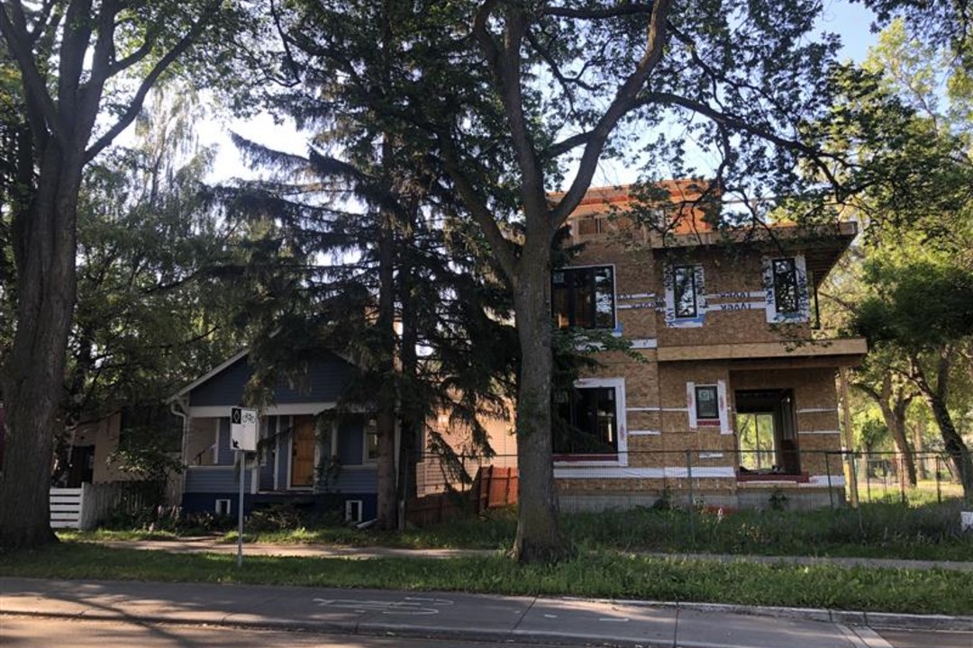 A house is under construction next to a smaller, older blue house.