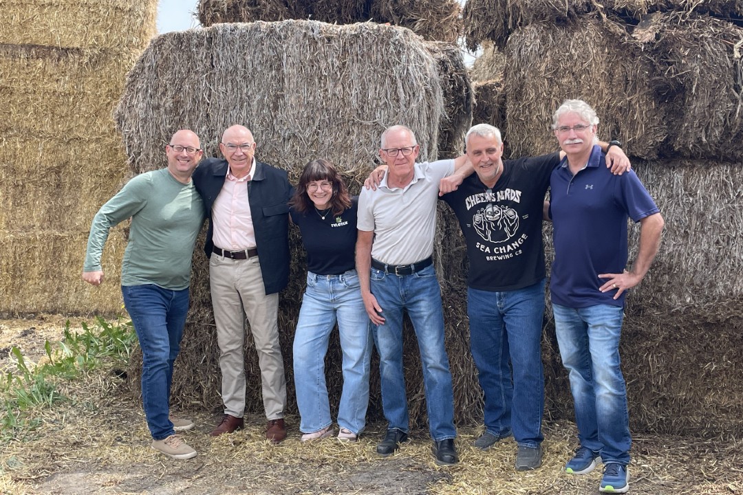 Five people link arms in front of bales of hemp.