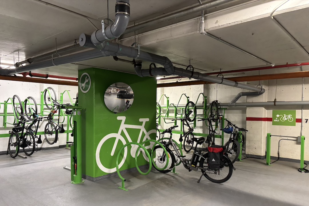 A bike storage area inside a parkade. The centre pillar is lime green and has a simple picture of a bike. The bike racks are also lime green and there is a sign pointing towards ebike chargers