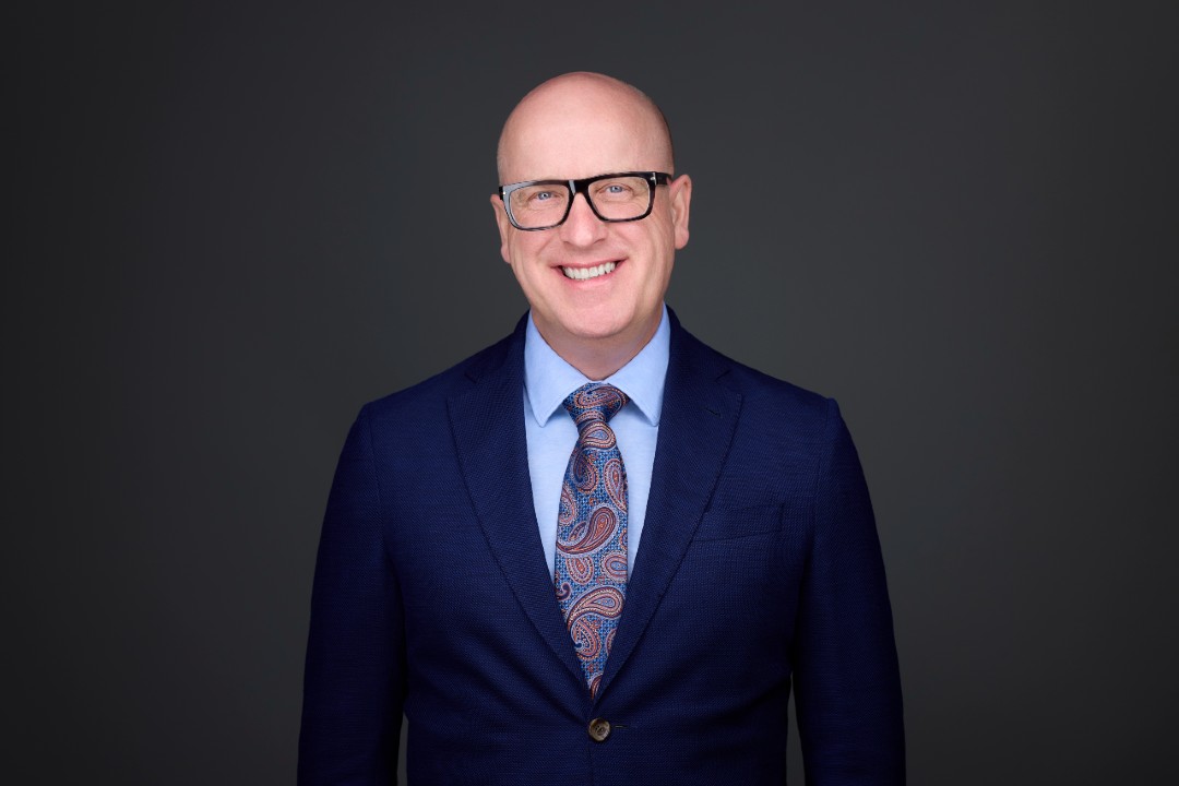 A smiling man wearing glasses and a navy blue print.