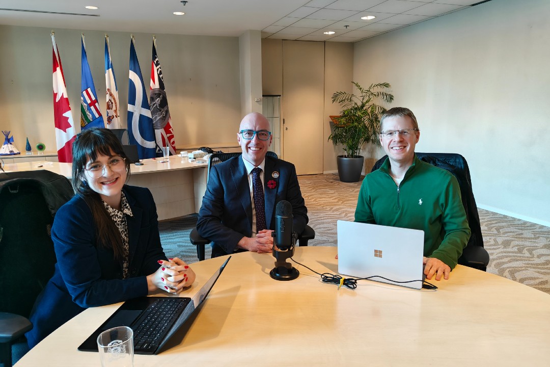 A woman and two men sit at a table with podcasting equipment.