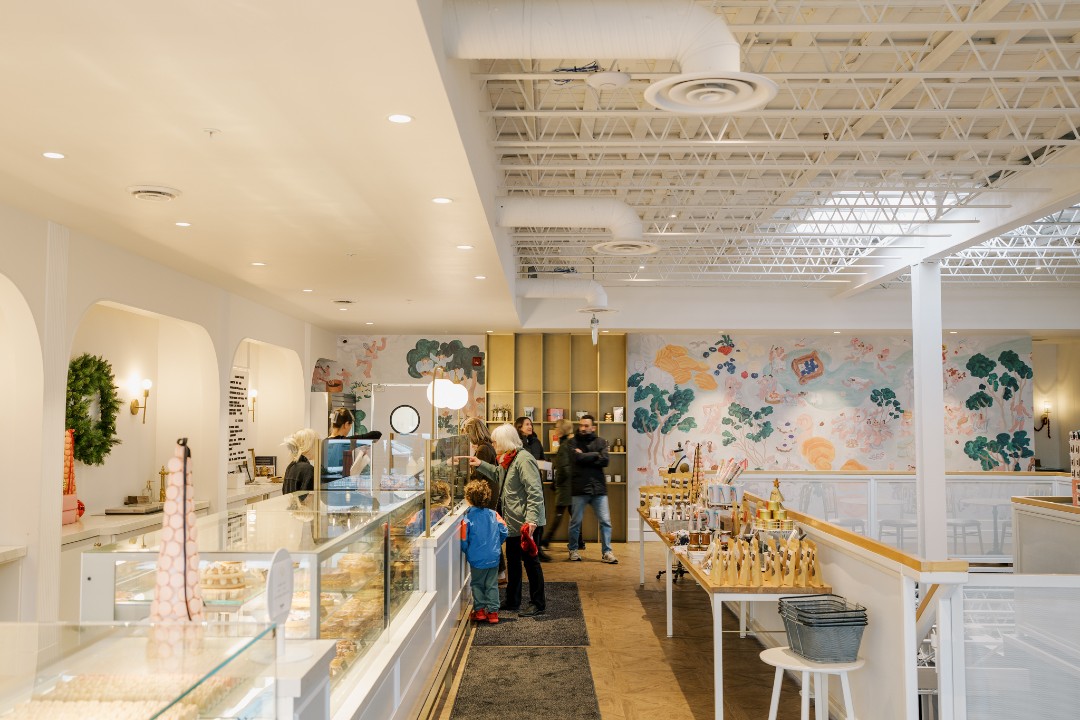 The mostly white interior of Duchess Bake Shop, where customers of varying ages gather at a glass display case.