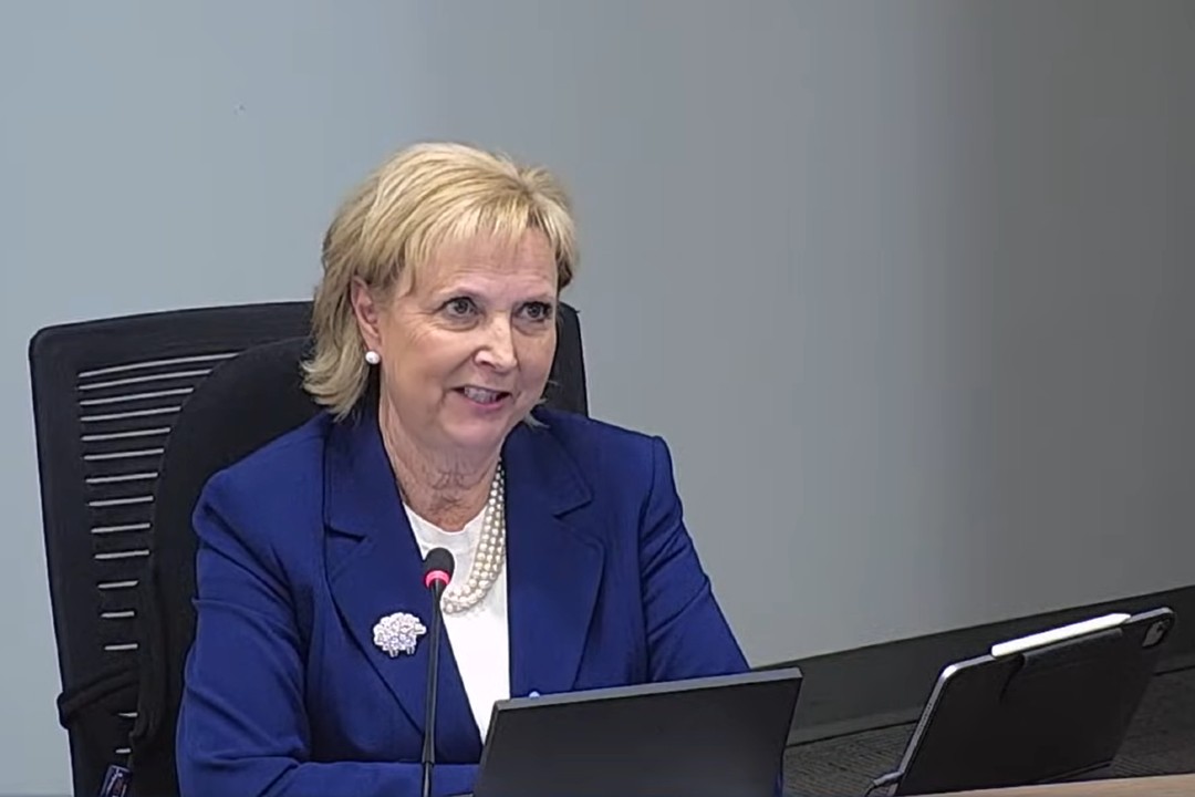 A woman wearing a blue blazer seated in a chair next to a microphone
