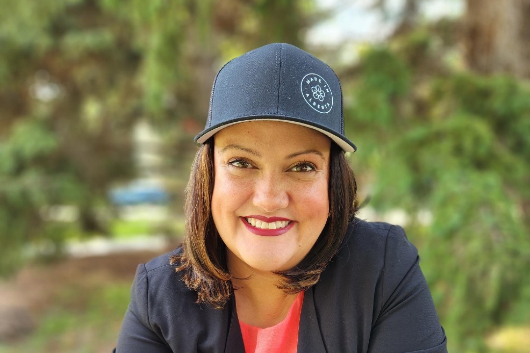 A smiling woman wearing a black hat emblazoned with the Made in Alberta logo.