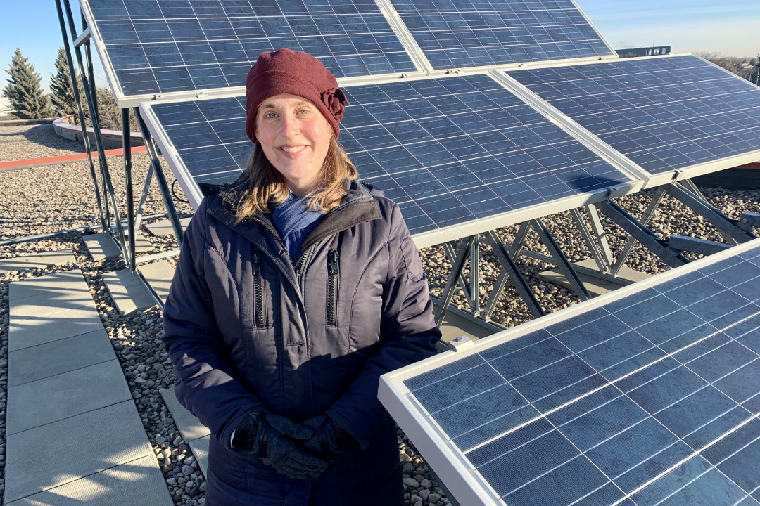 A smiling woman stands beside solar panels