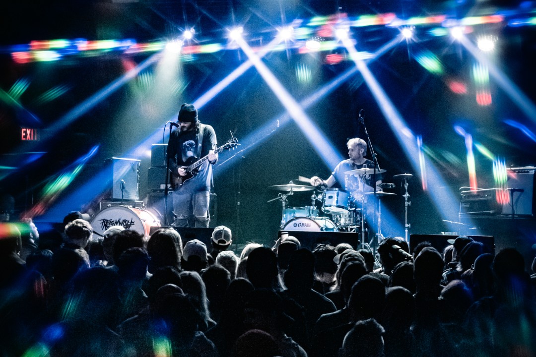 A band performs to an audience bathed in spotlights.