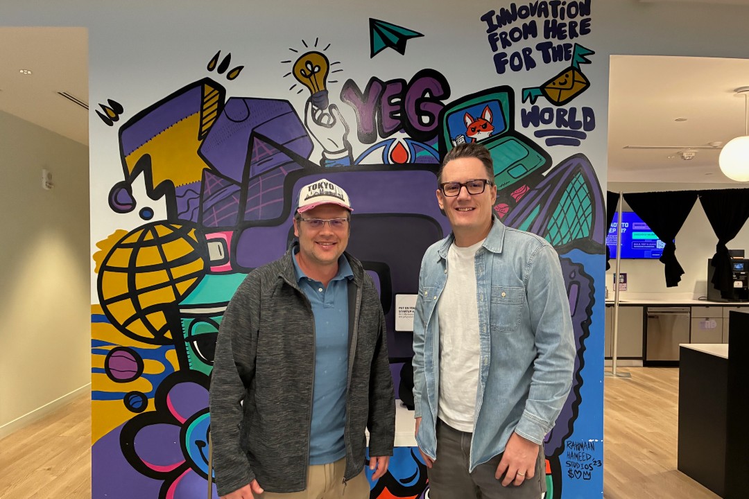 Two men pose in front a graffiti wall