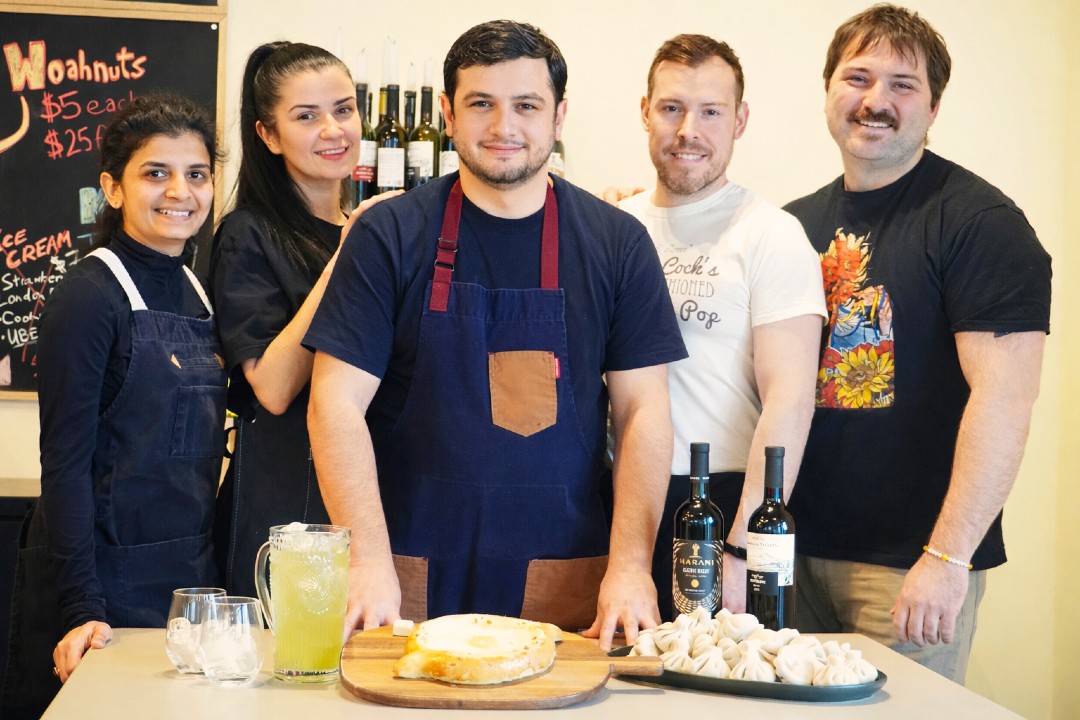 Five people gathered behind a spread of Georgian food and drink.