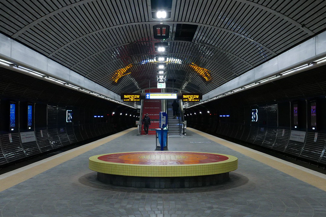 A round bench edged with bright yellow tiles on the platform at Bay/Enterprise Square LRT station