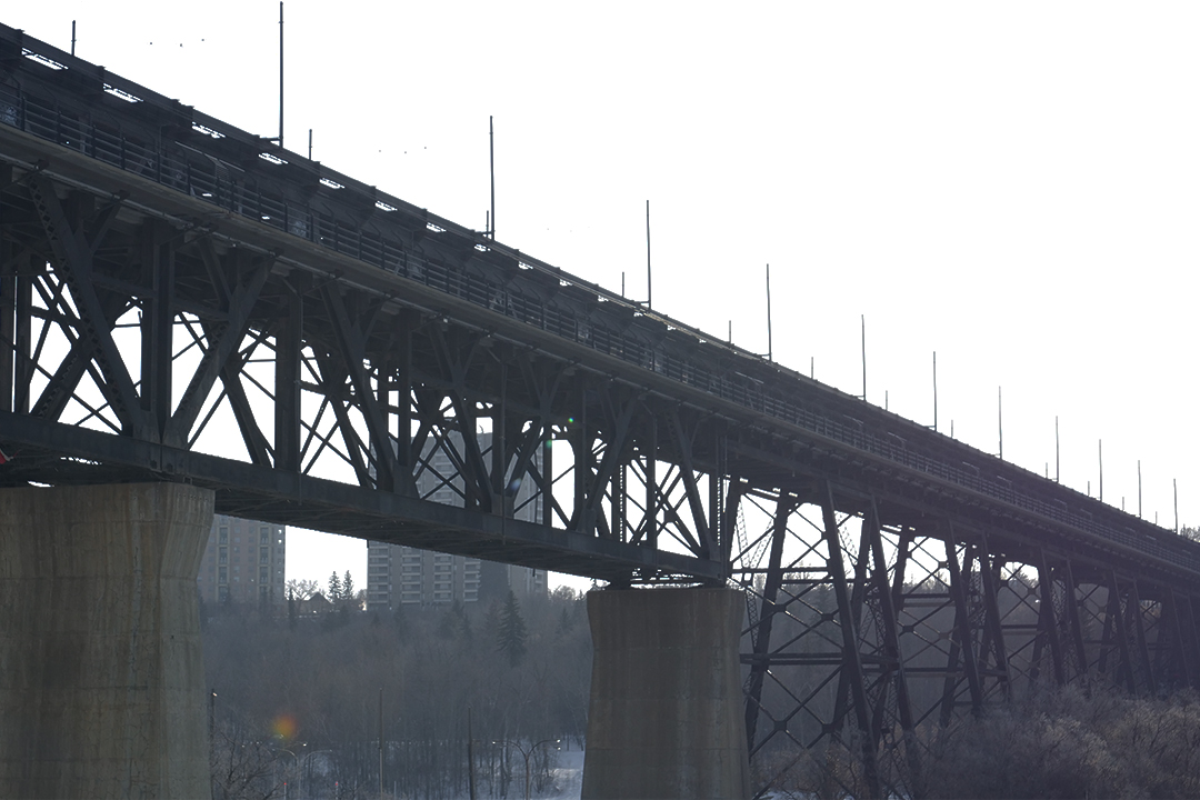 A brown, rusty steel truss bridge over the North Saskatchewan River.