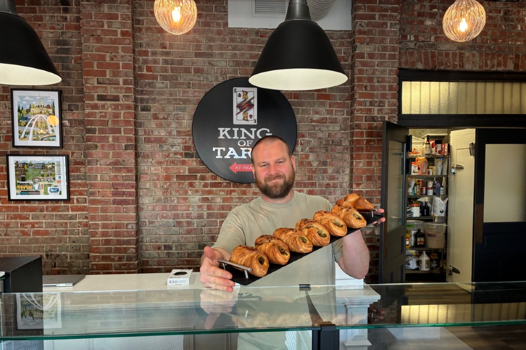 A man holds up a tray of pastries inside a bakery.