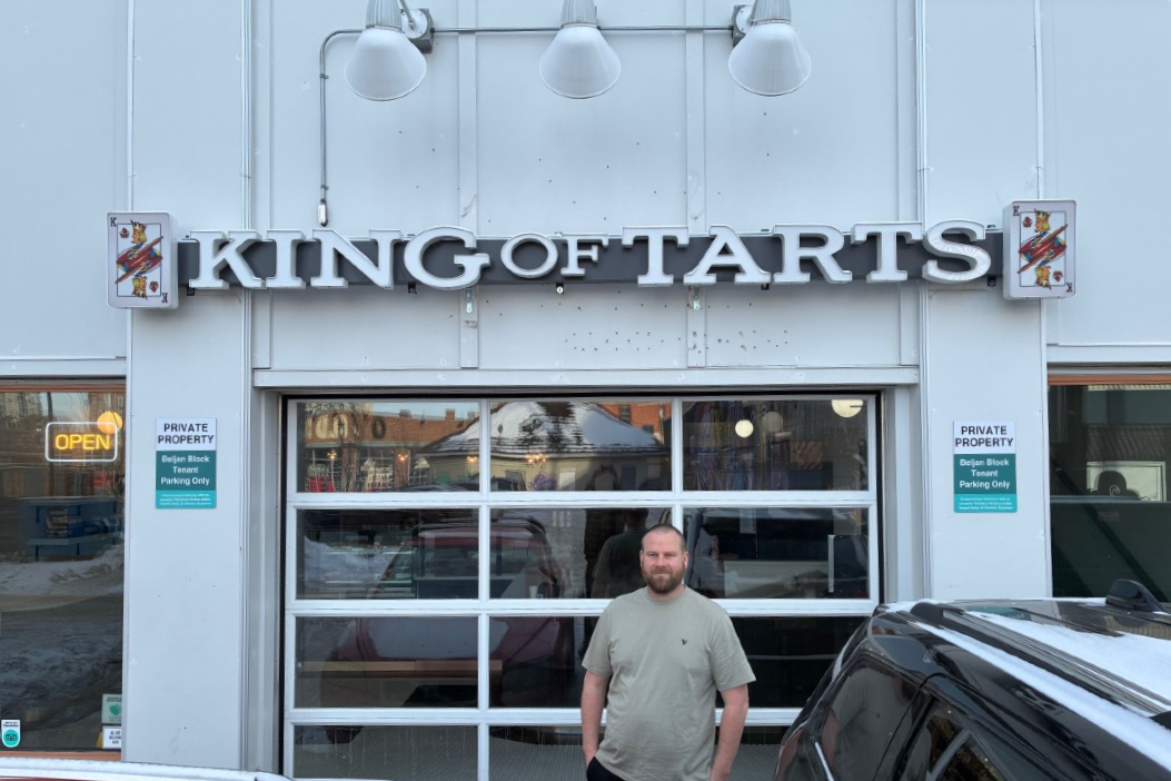 A man standing in front of a business with a sign that says King of Tarts.