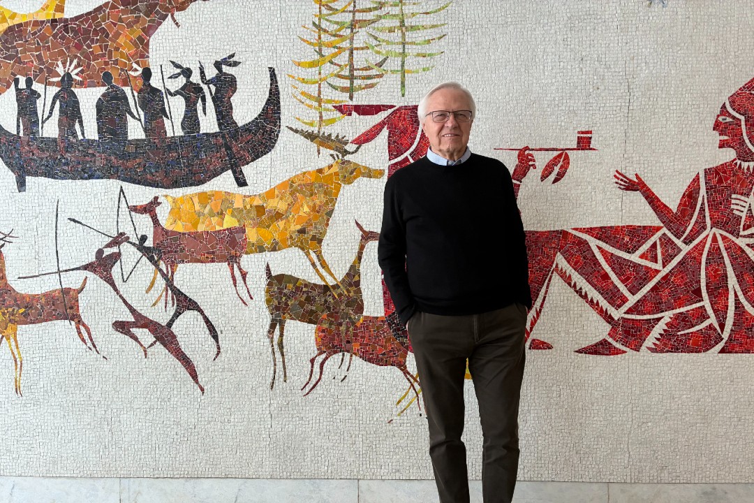 A man stands in front of a mosaic mural.