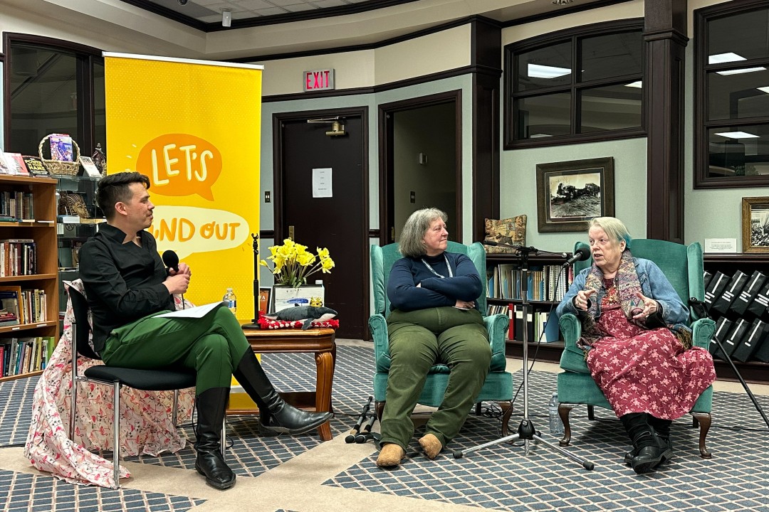 Three people sit in chairs in front of microphones.