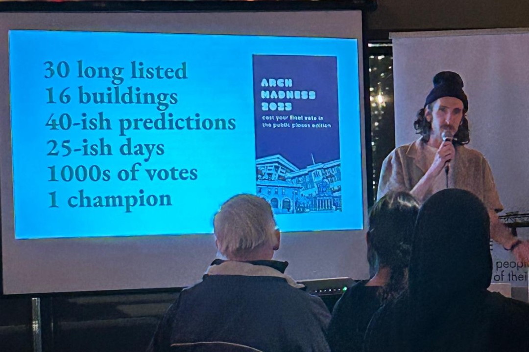 A man speaking to an audience next to a slide about Arch Madness.