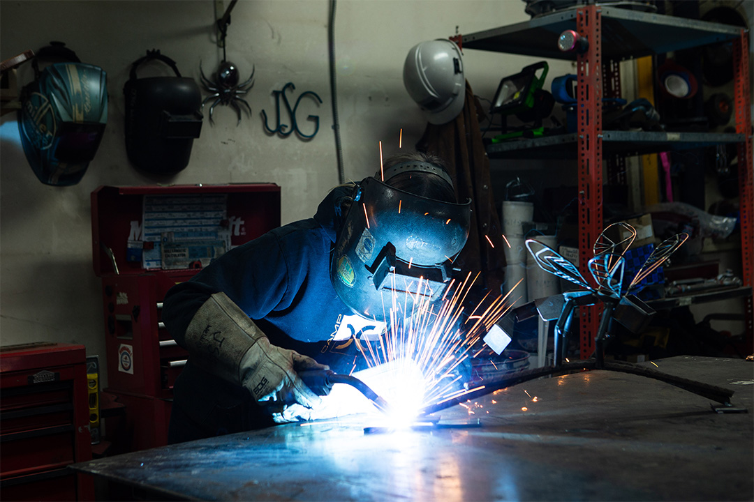 Sparks fly as a welder works on a steel bar with what looks like a flower sculpture on it