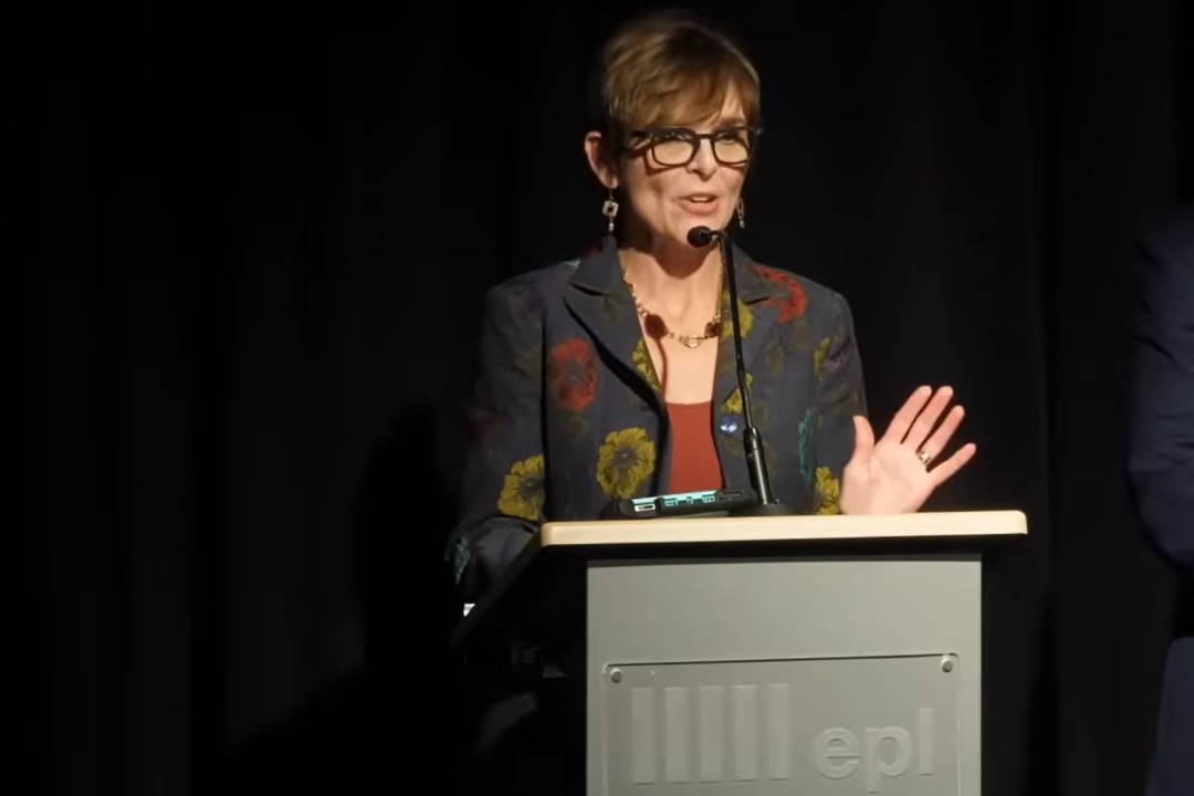 A woman speaks at a podium with the Edmonton Public Library logo on it