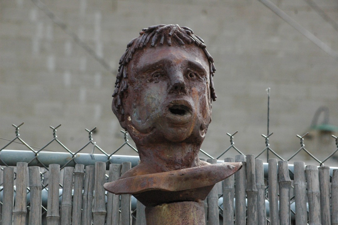 The head of a statue on a podium in front of a chain-link fence