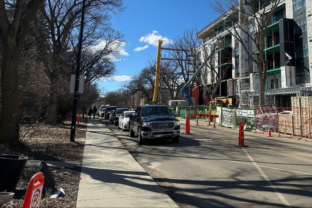 Vehicles queue on a two-lane road next to a construction site.