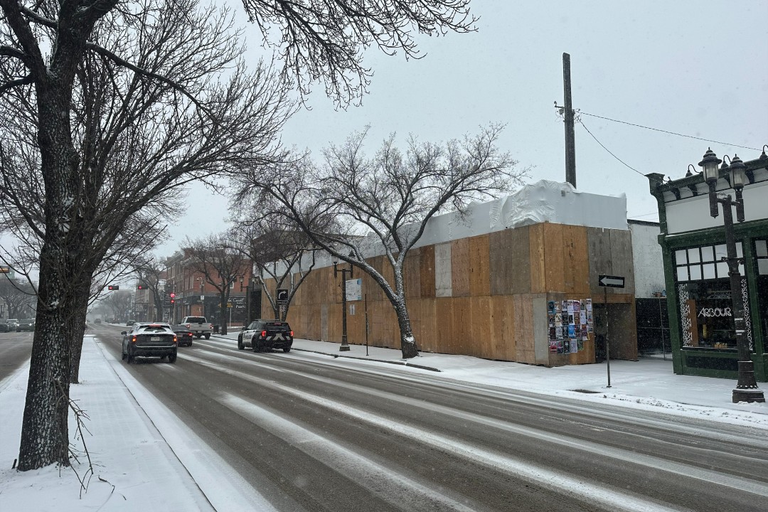 A building on Whyte Avenue covered in plywood on a snowy day.