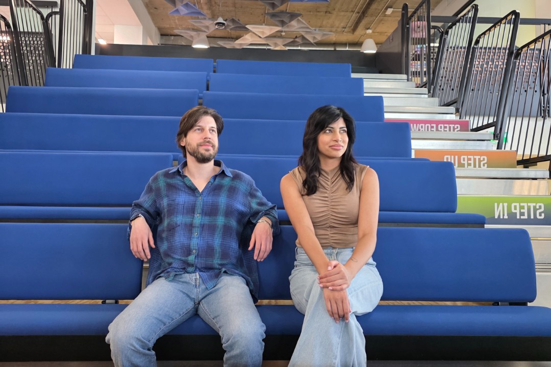 Two people look to the right while seated on bleachers.