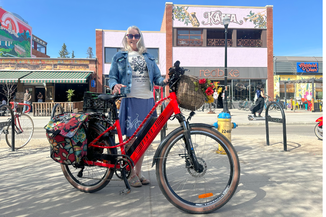 A woman poses with her red, decorated bicycle, in front of a cafe and bike shop.