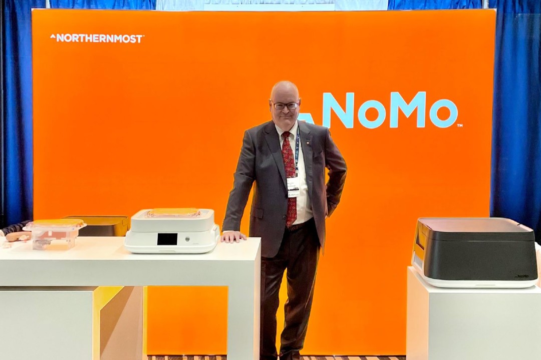 A man wearing a suit poses in front of a bright orange backdrop that reads Northernmost and NoMo
